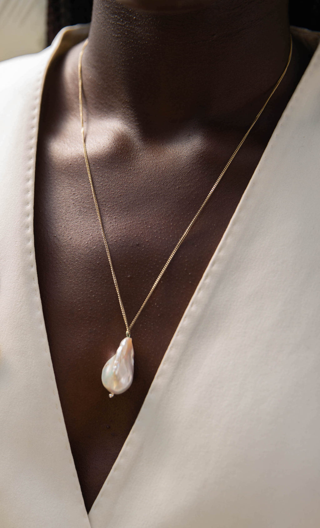 Model wearing handcrafted pearl necklace around neck, wearing a white blazer