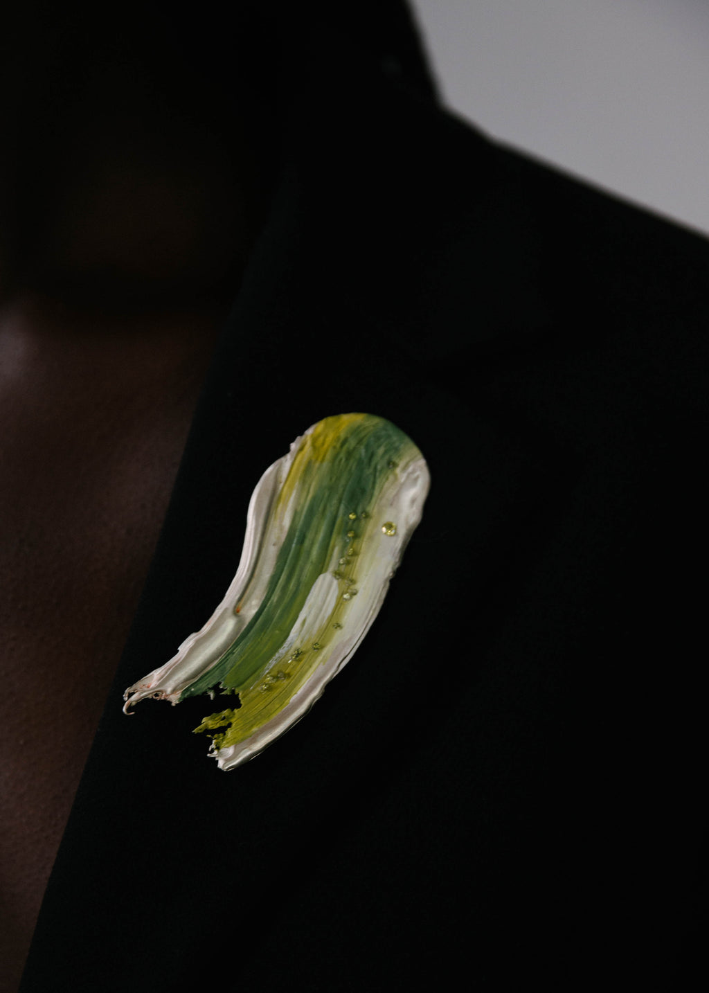 Close up of a silver handcrafted brooch with green elements painted on it