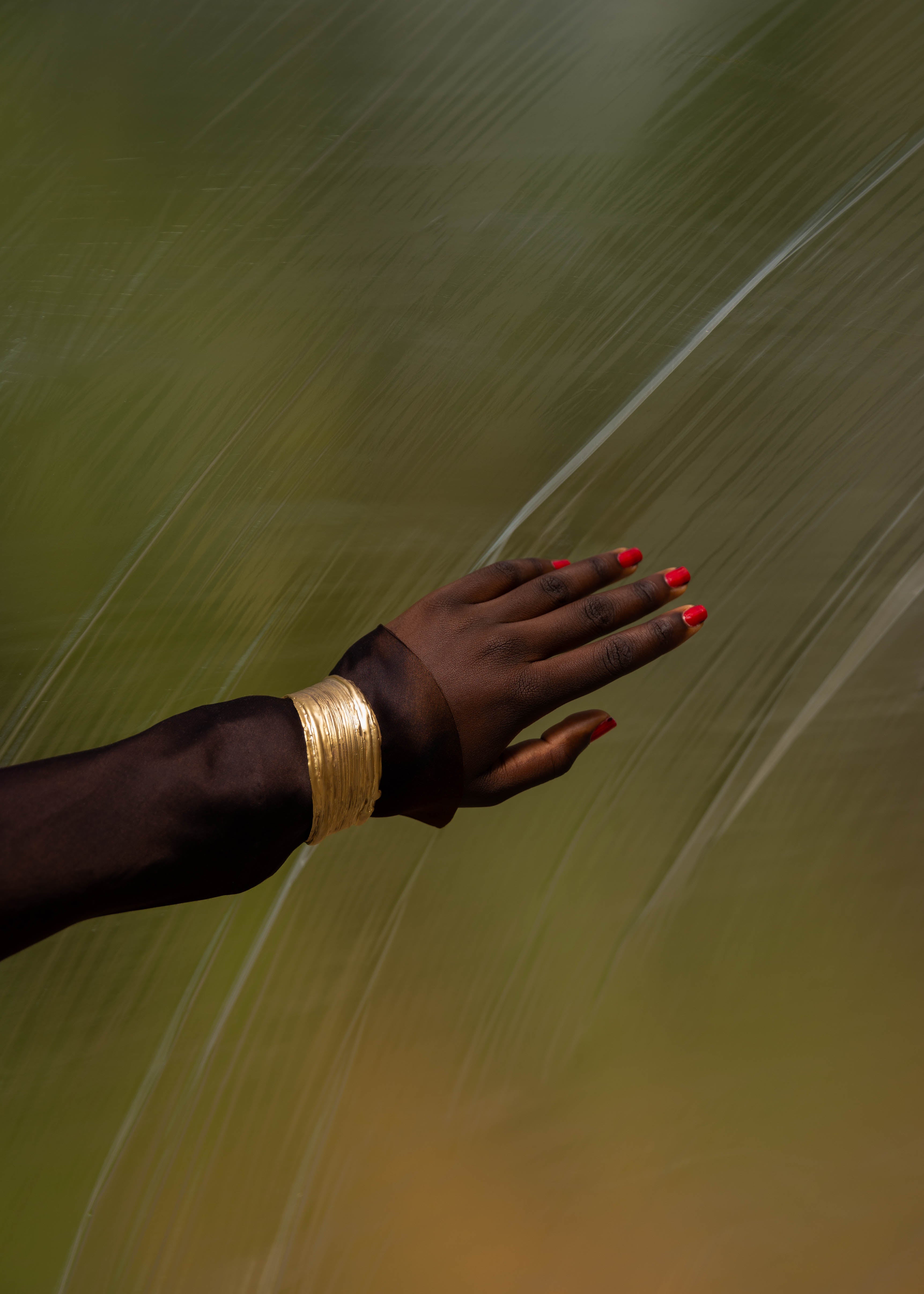 Hand with handcrafted gold bracelet and red nail polish against a blurred natural background