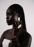 Woman wearing large handcrafted silver earrings and ring against a plain background