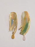 handcrafted gold earrings with mutiple colours painted on top, including green, salmon, light blue and white. Two gemstones are hanging from the bottom , one amber and the other quartz