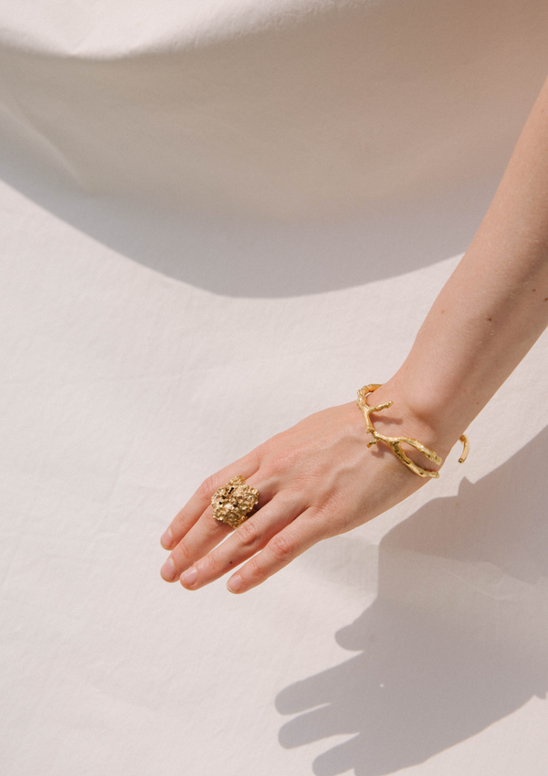handcrafted gold bracelet looking like a branch being worn by model w handcrafted gold ring in front of white background