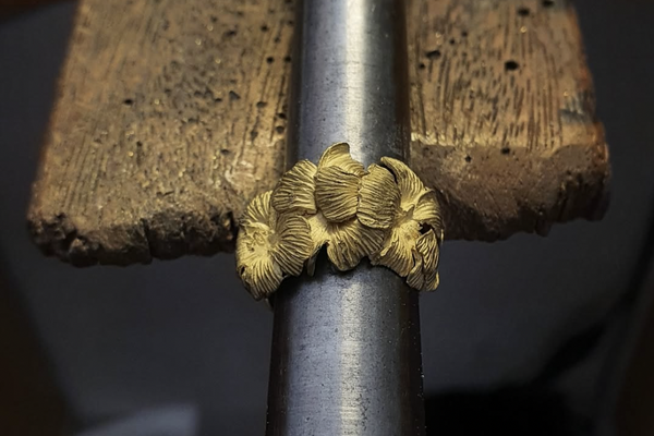 handcrafted Gold floral ring on a metal rod with a wooden anvil background