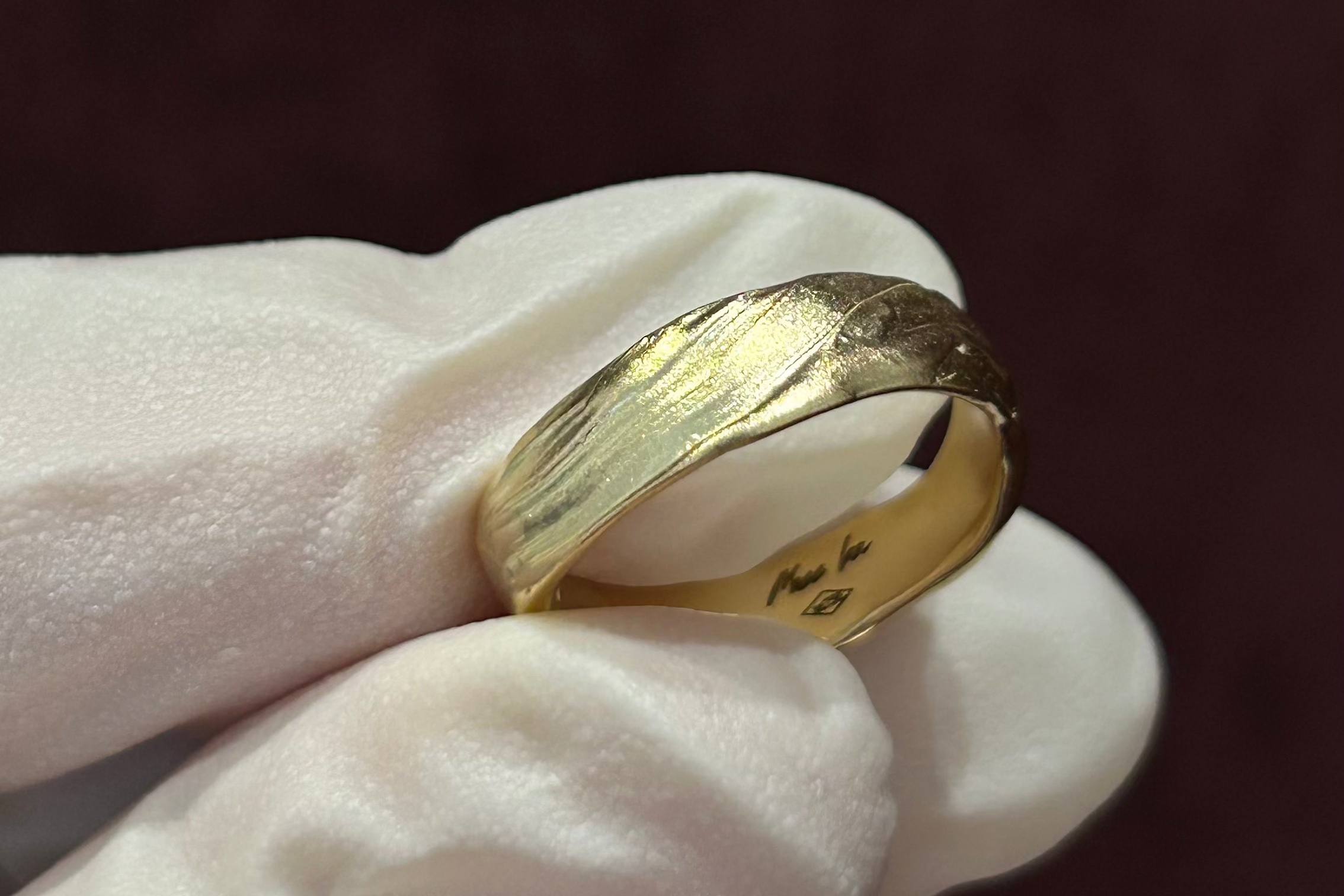 handcrafted custom Gold ring held by a gloved hand against a dark background