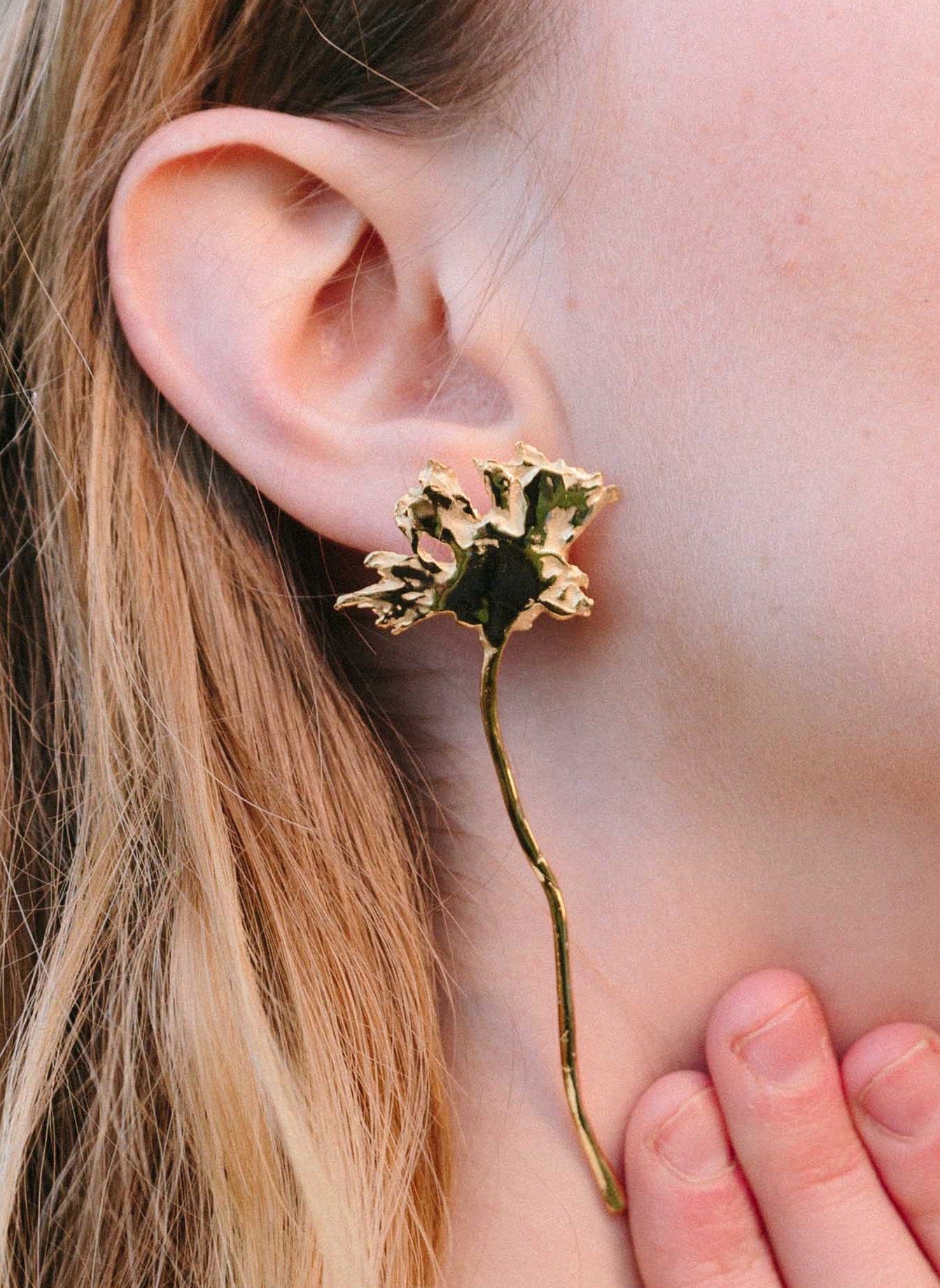 Close-up of a model wearing handcrated gold daisy earrings on her right ear