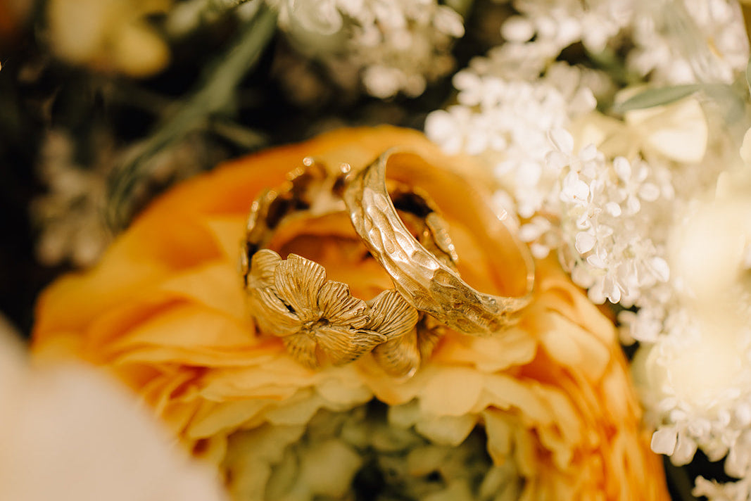 handcrafted Gold wedding rings on a bouquet of flowers with a blurred background