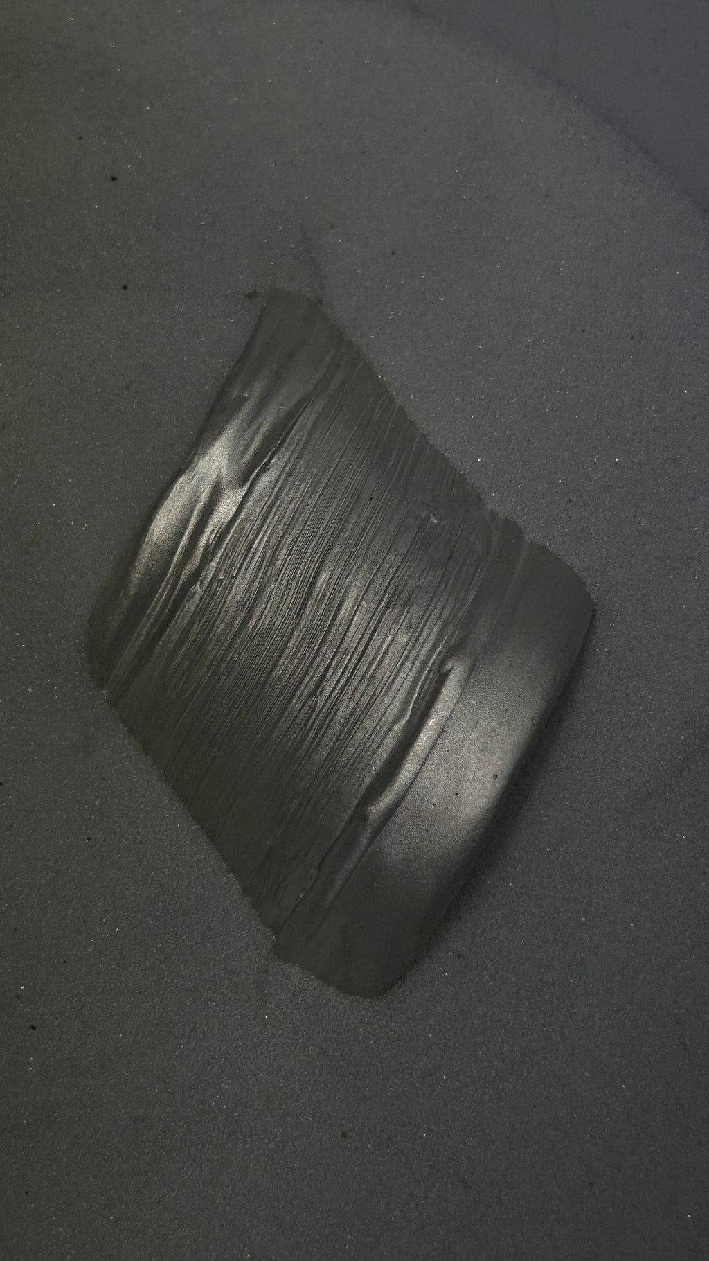 A dark gray metallic cylindrical sleeve or collar with a ribbed painted texture, photographed in white sand.