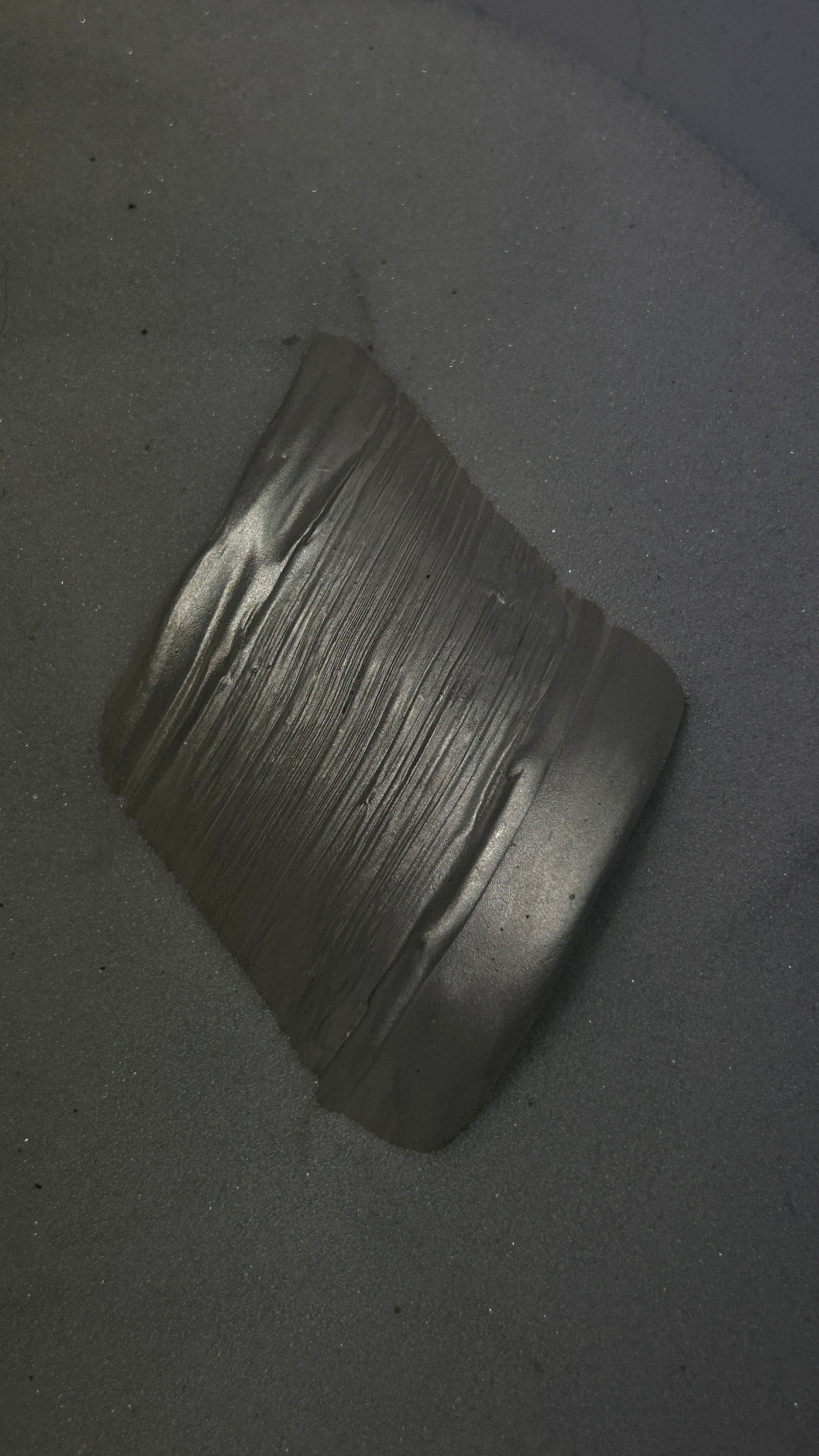 A dark gray metallic cylindrical sleeve or collar with a ribbed painted texture, photographed in white sand.
