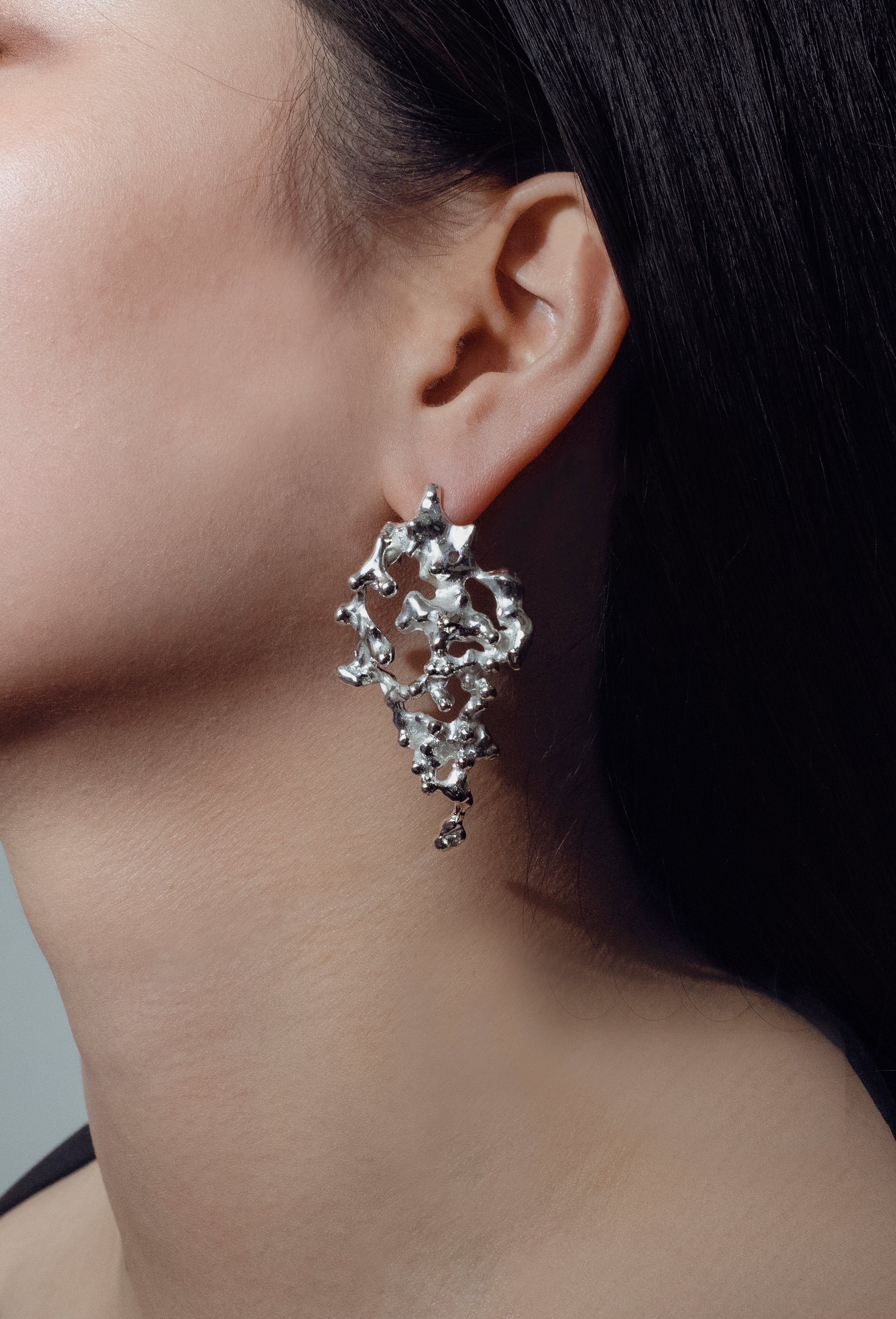Close-up of a person wearing a handcrafted silver earring with a detailed design.