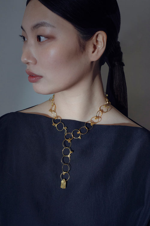 Woman wearing a handcrafted gold necklace against a neutral background
