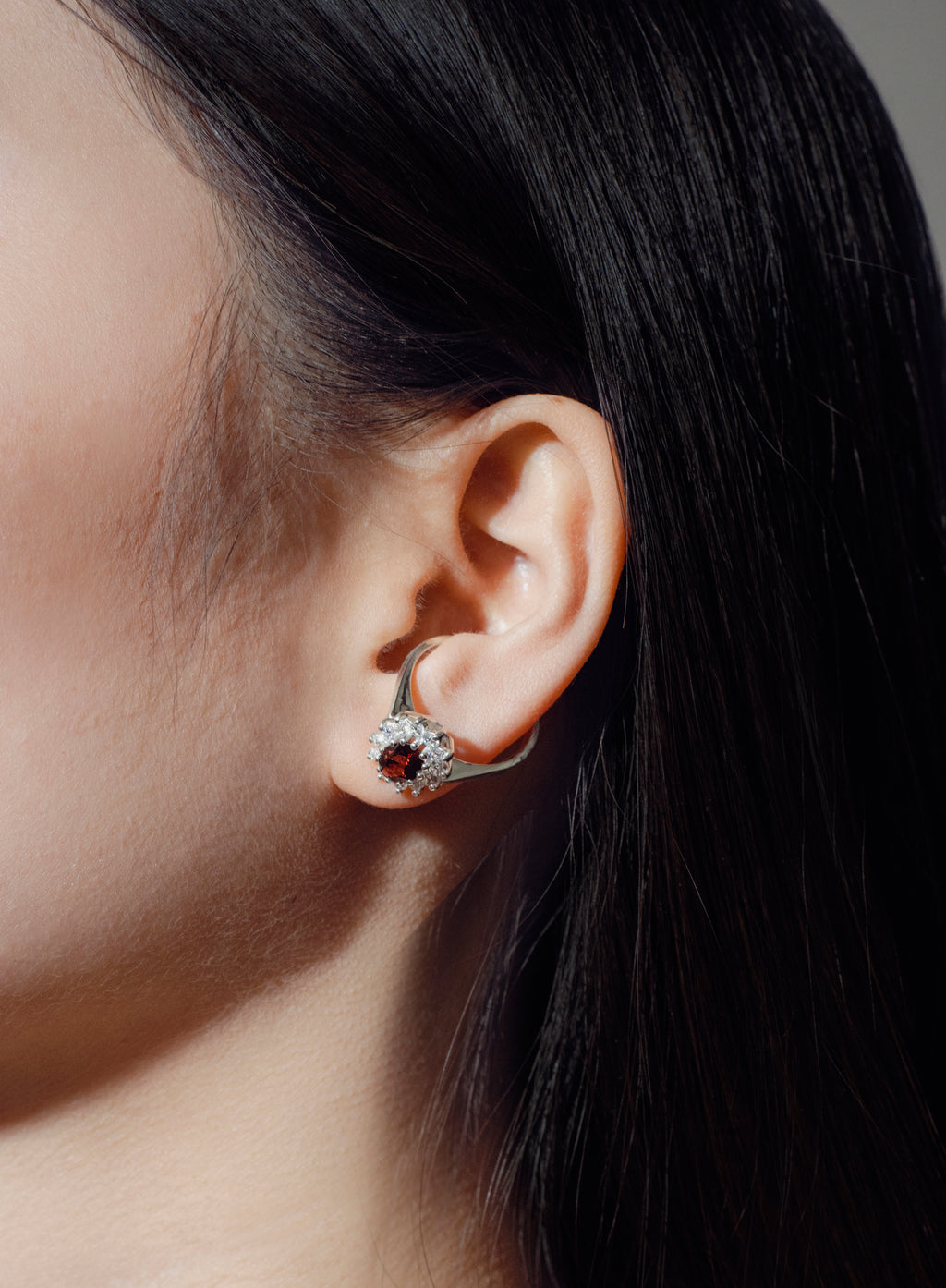 Close-up of an ear wearing a handcrafted silver earring with a red gemstone, dark hair in the background