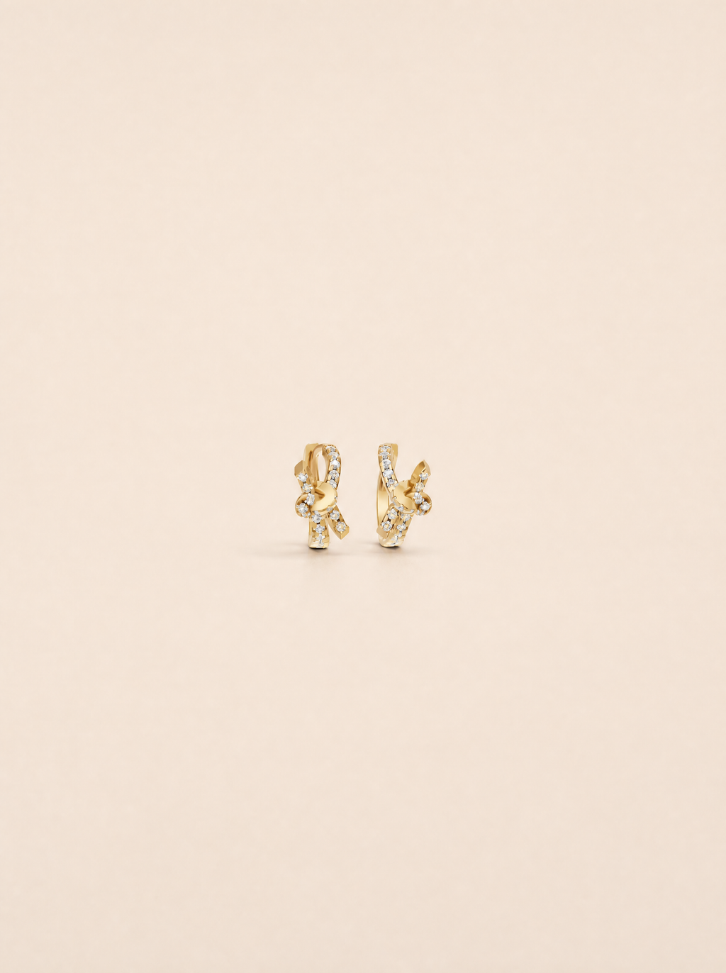 A pair of gold huggie hoop earrings with pavé-set clear stones, displayed on a solid light beige background.