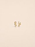 A pair of gold huggie hoop earrings with pavé-set clear stones, displayed on a solid light beige background.
