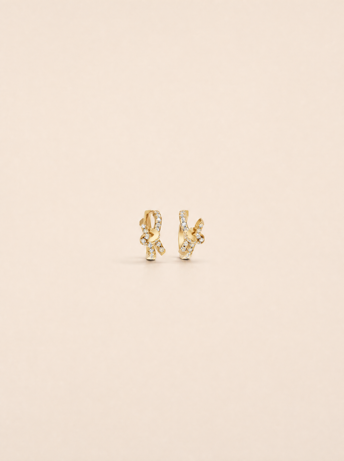 A pair of gold huggie hoop earrings with pavé-set clear stones, displayed on a solid light beige background.
