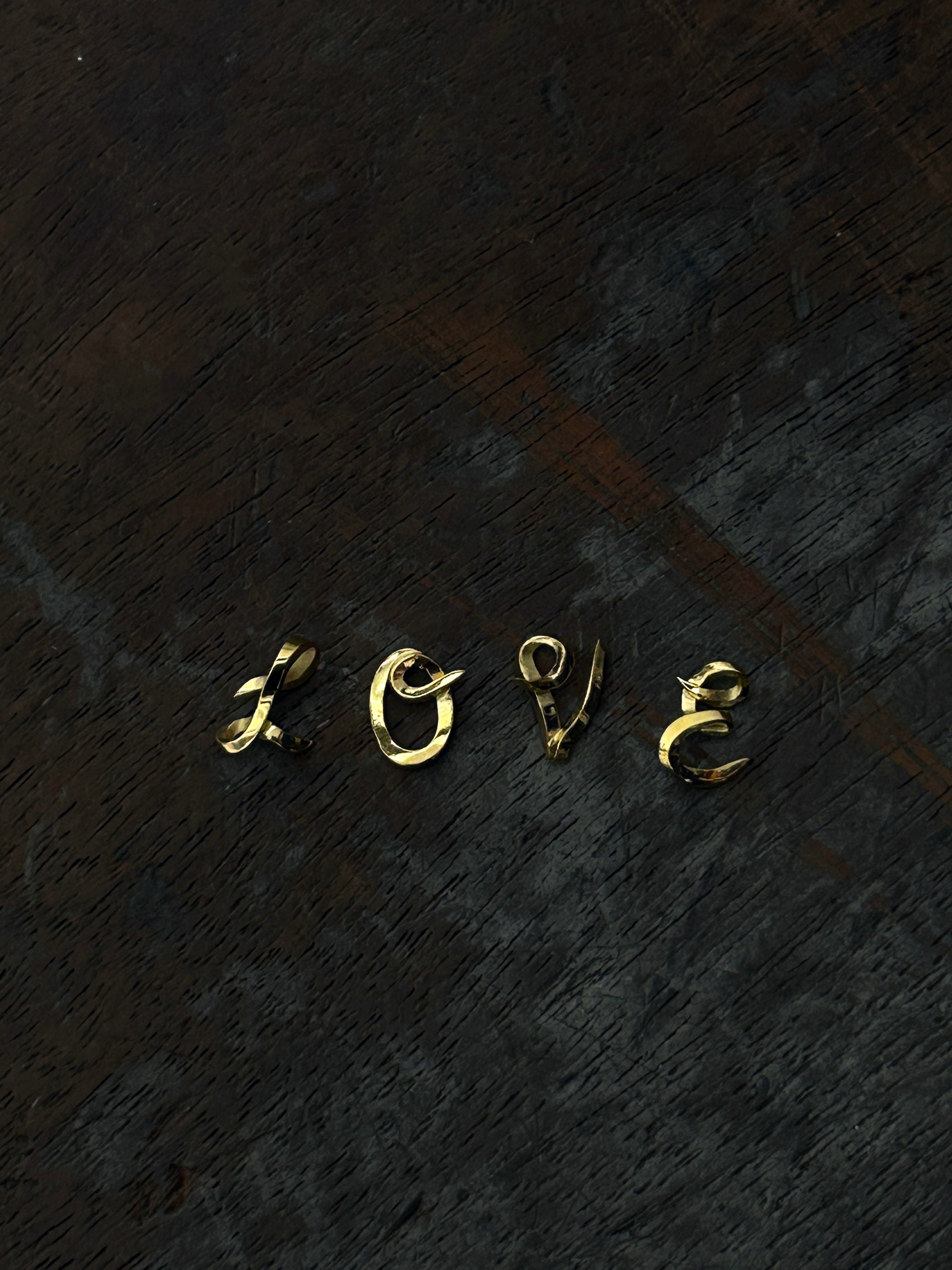 handcrafted Gold 'LOVE' letter charms on a dark textured surface
