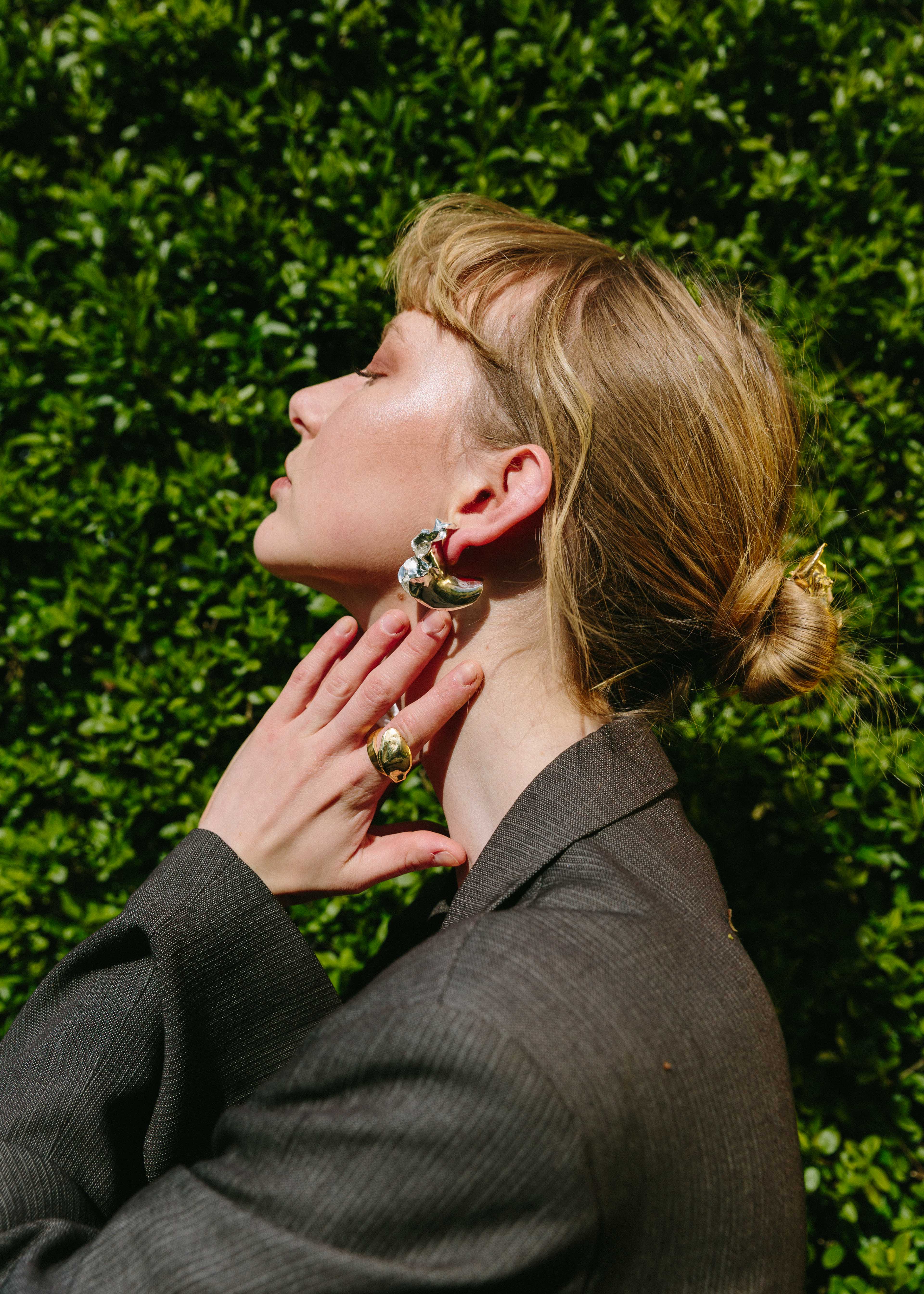Model adjusting her handcrafted silver orchid earrings against a green hedge background