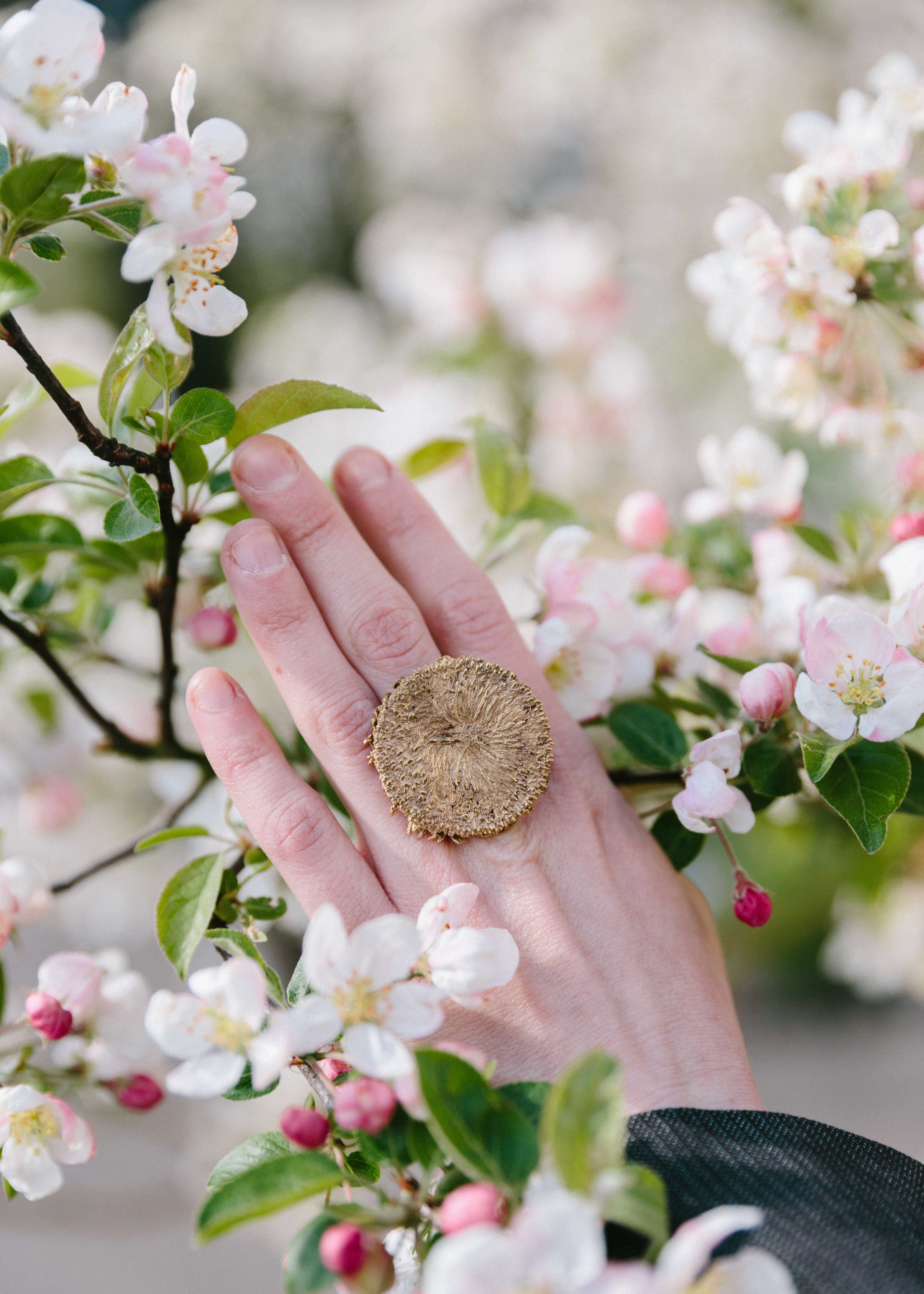 hand wearing the handcrafted helios ring with flower background