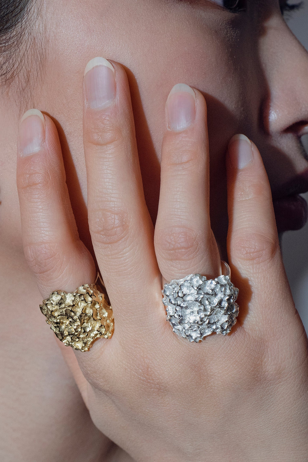 Close-up of model wearing handcrafted  gold and silver rings on a grey background
