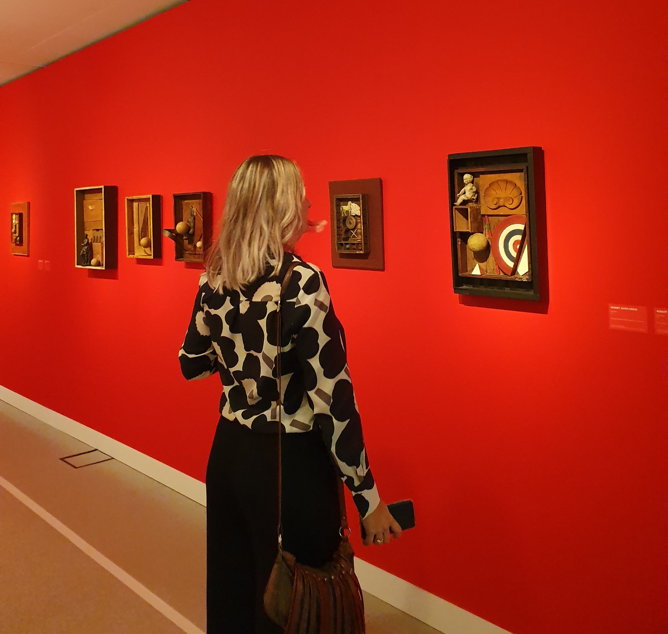 Woman standing in front of a red wall with framed artworks